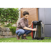 Eine Frau hockt im Garten und inspiziert einen Rasenlüfter.