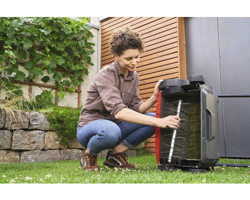 Eine Frau hockt im Garten und inspiziert einen Rasenlüfter.