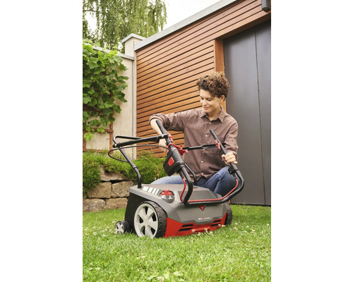 Eine Frau bedient einen Vertikutierer im Garten.