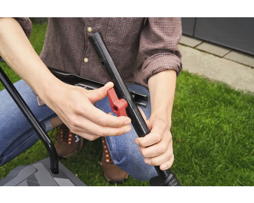 Eine Person montiert den Griff eines Rasenmähers mit einem roten Knopf.