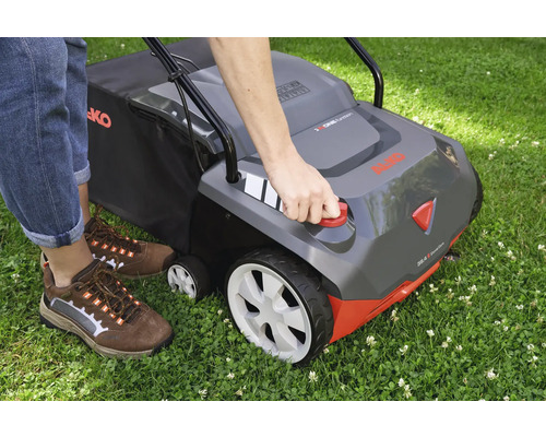 Eine Person bedient einen Vertikutierer auf einer Rasenfläche.