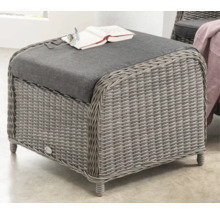 Tabouret de fauteuil de jardin tressé avec coussin en tissu gris, livre et lunettes.