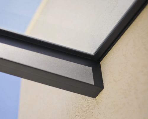 Détail d'un cadre en aluminium sombre pour une toiture de terrasse avec élément en verre sur un mur extérieur.