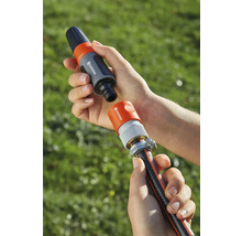 Zwei Hände halten Gardena Schlauchverbinder über einem Gartenschlauch.