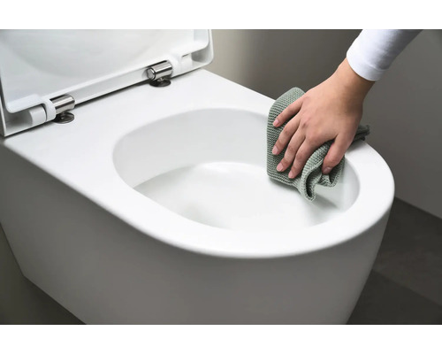 Eine Person reinigt eine weisse Hänge-Toilette mit einem Tuch.