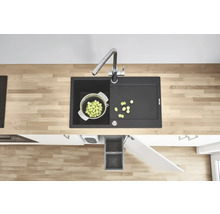 Évier de cuisine avec égouttoir, robinet, passoire à légumes et poubelle dans une cuisine moderne.