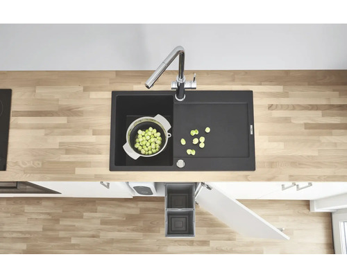 Évier de cuisine avec égouttoir, robinet, passoire à légumes et poubelle dans une cuisine moderne.