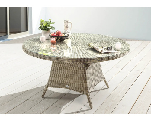 Table de jardin ronde avec plateau en verre et socle tressé sur une terrasse.