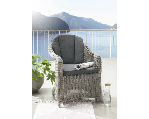 Geflochtener Sessel mit Kissen und Zeitungsrolle auf einem Balkon mit Seeblick