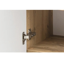 Gros plan d'une charnière de meuble en métal montée sur une porte d'armoire blanche et un intérieur aspect bois.