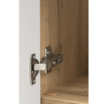 Charnière métallique pour meuble montée sur une porte blanche et un corps en bois.