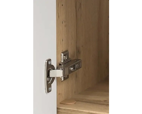 Charnière métallique pour meuble montée sur une porte blanche et un corps en bois.