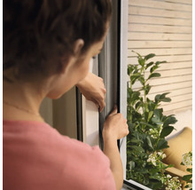 Frau montiert ein Insektenschutzgitter am Fenster.