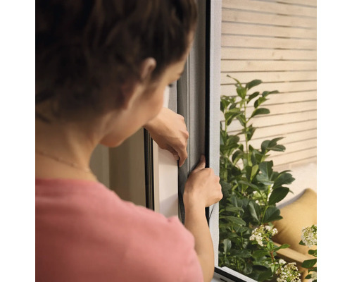 Frau montiert ein Insektenschutzgitter am Fenster.