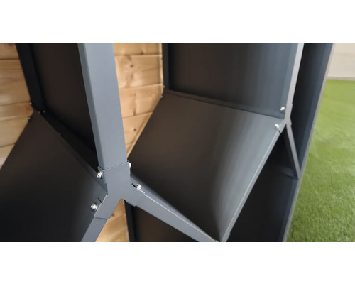 Vue détaillée d'un raccord d'angle en métal gris pour un abri de jardin avec des vis apparentes devant une paroi en bois.