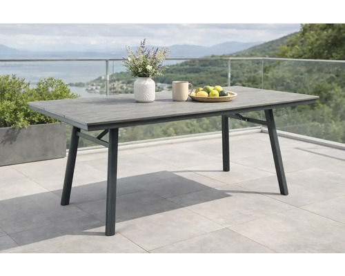 Table de jardin moderne avec plateau aspect bois et cadre en métal sur une terrasse avec rambarde en verre et vue sur le lac et les montagnes.