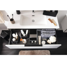 Moderner weisser Waschtisch mit geöffneter Schublade, Schubladen-Organisationssystem mit Toilettenartikeln und hellbraune Badematte.