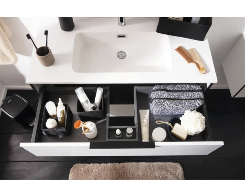 Moderner weisser Waschtisch mit geöffneter Schublade, Schubladen-Organisationssystem mit Toilettenartikeln und hellbraune Badematte.