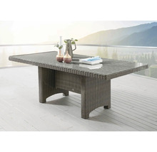 Table de jardin rectangulaire en polyrotin avec plateau en verre sur une terrasse lumineuse devant un paysage de montagne.