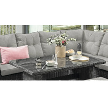 Salon de jardin en polyrotin avec canapé gris et table à plateau en verre, décoré avec de la vaisselle et des fleurs sur une terrasse.