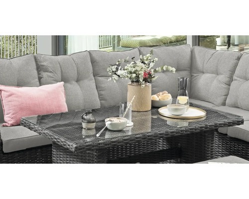 Salon de jardin en polyrotin avec canapé gris et table à plateau en verre, décoré avec de la vaisselle et des fleurs sur une terrasse.