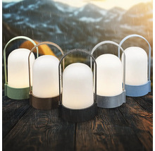 Cinq lanternes LED d extérieur portables de différentes couleurs sur une table en bois sous la pluie avec des montagnes en arrière-plan.