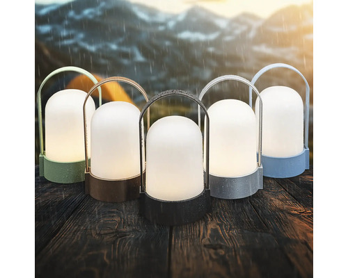 Cinq lanternes LED d extérieur portables de différentes couleurs sur une table en bois sous la pluie avec des montagnes en arrière-plan.