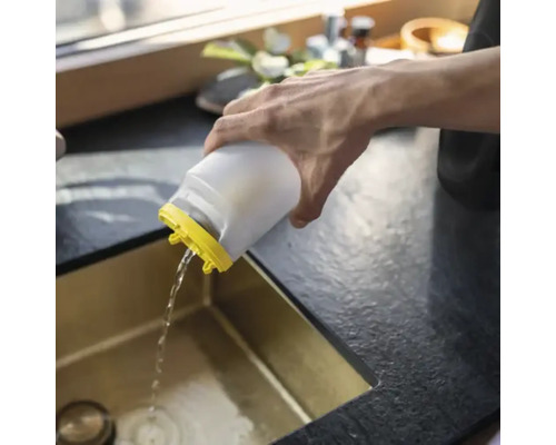 Une personne verse de l'eau d'un récipient en plastique blanc avec un couvercle jaune dans un évier de cuisine doré.