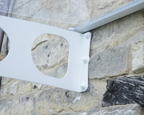 Support métallique blanc pour un auvent, monté sur un mur en pierre naturelle avec des vis apparentes.