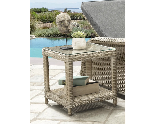 Quadratischer Beistelltisch aus Polyrattan mit Glasplatte und Ablagefläche auf einer hellen Terrasse am Pool neben einer Gartenliege.