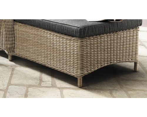 Detailaufnahme eines Gartenmöbels aus Polyrattan mit dunklem Sitzkissen auf Steinboden.