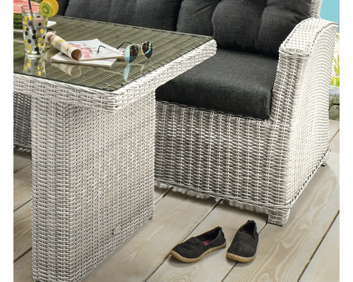Ensemble de jardin en résine tressée claire avec table en verre et fauteuil lounge aux coussins foncés sur une terrasse en bois.