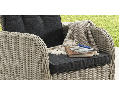 Fauteuil de jardin en résine tressée avec coussins, un plaid à chevrons, un carnet de notes, une photo et un stylo.