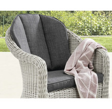 Fauteuil de jardin en polyrotin avec coussins d'assise et de dossier foncés et un plaid rayé dans un jardin.