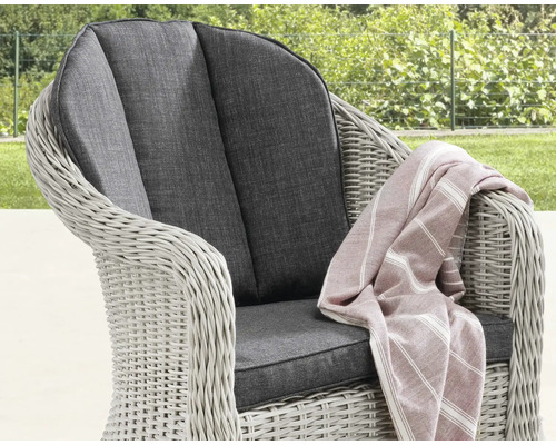 Fauteuil de jardin en polyrotin avec coussins d'assise et de dossier foncés et un plaid rayé dans un jardin.