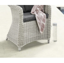 Fauteuil de jardin tressé style rotin avec coussins, une couverture à rayures et une bouteille d'eau dans un espace extérieur lumineux.