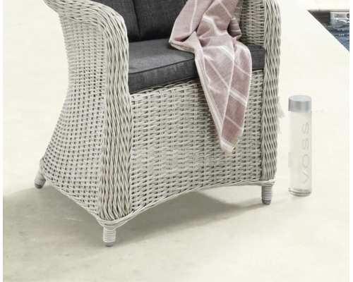 Fauteuil de jardin tressé style rotin avec coussins, une couverture à rayures et une bouteille d'eau dans un espace extérieur lumineux.