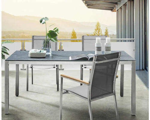Ensemble de jardin moderne sur balcon avec table rectangulaire, plateau gris foncé, cadre en métal et chaises en maille avec accoudoirs en bois.