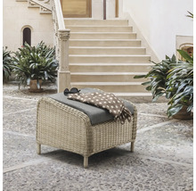 Pouf de jardin en résine tressée avec coussin gris sur une terrasse pavée devant un escalier en pierre.