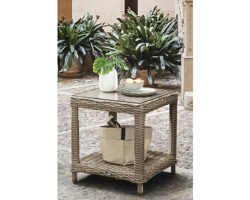 Table d appoint de jardin carrée en polyrotin gris avec plateau en verre et étagère de rangement, décorée d un vase et d un bol sur une terrasse.