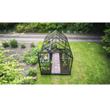 Serre en verre autoportante avec cadre noir et toit à deux versants dans un jardin avec des plantes et une allée pavée.