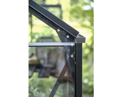 Gros plan d'un raccord d'angle sur le cadre d'une serre en aluminium noir avec des vitres et des vis de fixation.