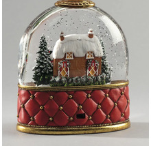 Schneekugel mit winterlichem Haus, verschneiten Tannen und rotem, gestepptem Sockel mit goldfarbenen Details.