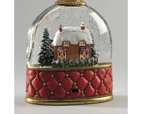Schneekugel mit winterlichem Haus, verschneiten Tannen und rotem, gestepptem Sockel mit goldfarbenen Details.
