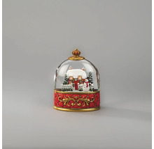 Schneekugel mit verschneitem Haus, Schneemann und Tannenbäumen auf einem verzierten roten Sockel mit goldenen Ornamenten.