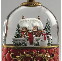 Schneekugel Weihnachtsdekoration mit verschneitem Haus, Schneemann und Tannen auf rotem Sockel mit goldenen Verzierungen.