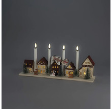 Décoration de Noël en bois avec village miniature, maisons illuminées, sapins, rennes et quatre bougies électriques blanches sur un socle.