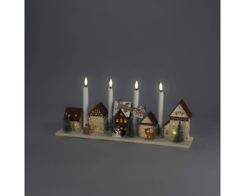 Décoration de Noël en bois avec village miniature, maisons illuminées, sapins, rennes et quatre bougies électriques blanches sur un socle.