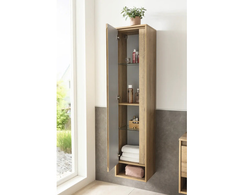 Armoire haute de salle de bains en décor bois, montage mural, porte ouverte laissant voir des étagères en verre avec accessoires et serviettes.