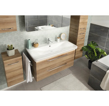 Ensemble de meubles de salle de bains moderne en aspect chêne avec lavabo blanc, armoires assorties, grand miroir et papier peint à motifs.